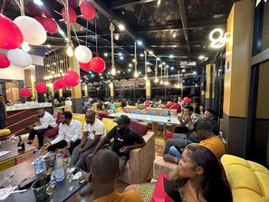 A spacious indoor venue with multiple seating areas, tables with drinks, and hanging decorations. - BLUE EMPIRE HOTEL (Buea)