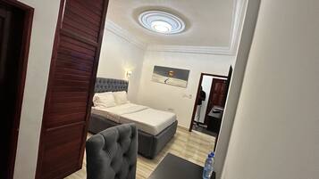 A hotel room with a bed, a sofa, a small table with a water bottle, and a ceiling light.