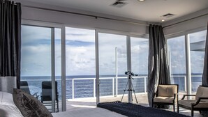 A modern hotel room with a large bed, a balcony with a telescope, and a view of the ocean. - Stunning Oceanfront 5 Bed House with Infinity Pool (West Bay)