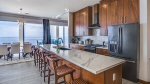 A modern kitchen with a large island, wooden cabinets, and a stainless steel refrigerator. - Stunning Oceanfront 5 Bed House with Infinity Pool (West Bay)