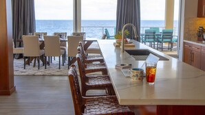 A kitchen with a view of the sea, a dining area with chairs, and a bar area with a laptop and a drink. - Stunning Oceanfront 5 Bed House with Infinity Pool (West Bay)