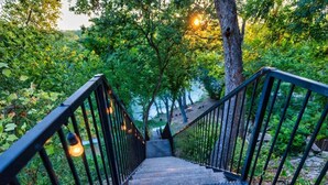 Una escalera con barandillas metálicas que baja hacia un cuerpo de agua, rodeada de follaje.
