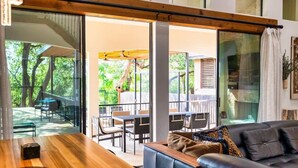 Una sala de estar moderna con una mesa de madera y un sofá de cuero, ventanas amplias con vistas a un patio exterior.