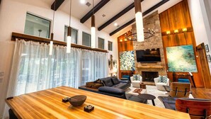 Una sala de estar moderna con una mesa de comedor de madera, una chimenea y un televisor grande montado en la pared.