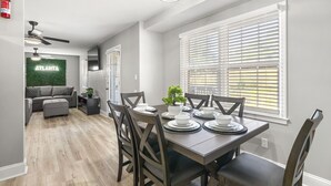 Ein Essbereich mit einem Tisch für vier Personen, umgeben von Stühlen, und ein Wohnbereich mit einer Couch und einer kleinen Pflanze.