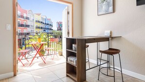 Ein Zimmer mit Holztisch und Barhocker, ein Balkon mit roten Stühlen und Blick auf farbenfrohe Gebäude.