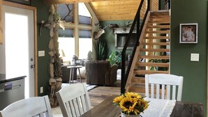 A dining area with a wooden table, white chairs, and a vase of sunflowers. A large antler chandelier hangs from the ceiling, and a deer head sculpture is mounted on the wall. - Three bedroom,  two bath on the Middle Fork of Rock Creek (Philipsburg)