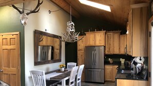 A kitchen with wooden cabinets, a stainless steel refrigerator, a dining table with chairs, and a chandelier. - Three bedroom,  two bath on the Middle Fork of Rock Creek (Philipsburg)