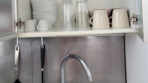 Cucina con lavello in acciaio inox, rubinetteria e portautensili. Sopra il lavello, mensole con diversi bicchieri e stoviglie.