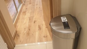 A hallway with a tiled floor, a trash bin, and a door leading to another room.