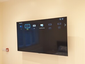 A flat-screen TV mounted on a wall with a source menu displaying various input options.