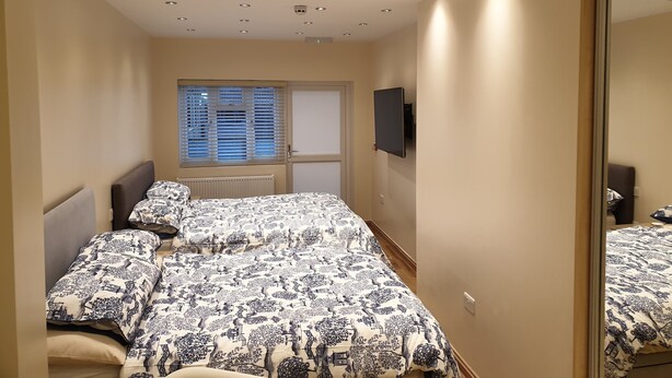 A bedroom with two beds, a large mirror, a TV mounted on the wall, and a window with blinds.