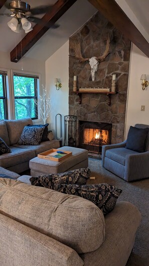 Cozy living room with a stone fireplace, comfortable seating area, and a window offering a view of the outdoors.
