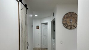 Un couloir doté d’un plancher en bois, de murs blancs, d’une horloge en bois et d’une porte coulissante de style rustique.