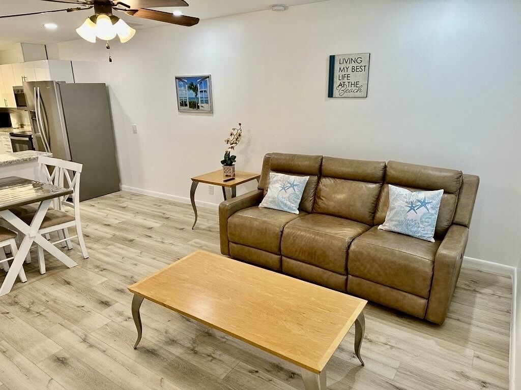 A living room with a brown leather sofa, a wooden coffee table, and a dining area with a white table and chairs.