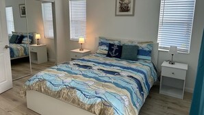 Une chambre à coucher avec un lit, des tables de chevet, un ventilateur de plafond et un grand miroir.