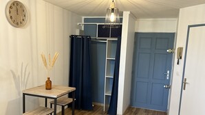 A room with a wooden floor, a table with two chairs, a blue door, and a wall-mounted clock. - Studio 5 mn des Plages (Schoelcher)