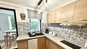 A modern kitchen with wooden cabinets, a dishwasher, a sink, and a window with a view of greenery. - Studio 5 mn des Plages (Schoelcher)