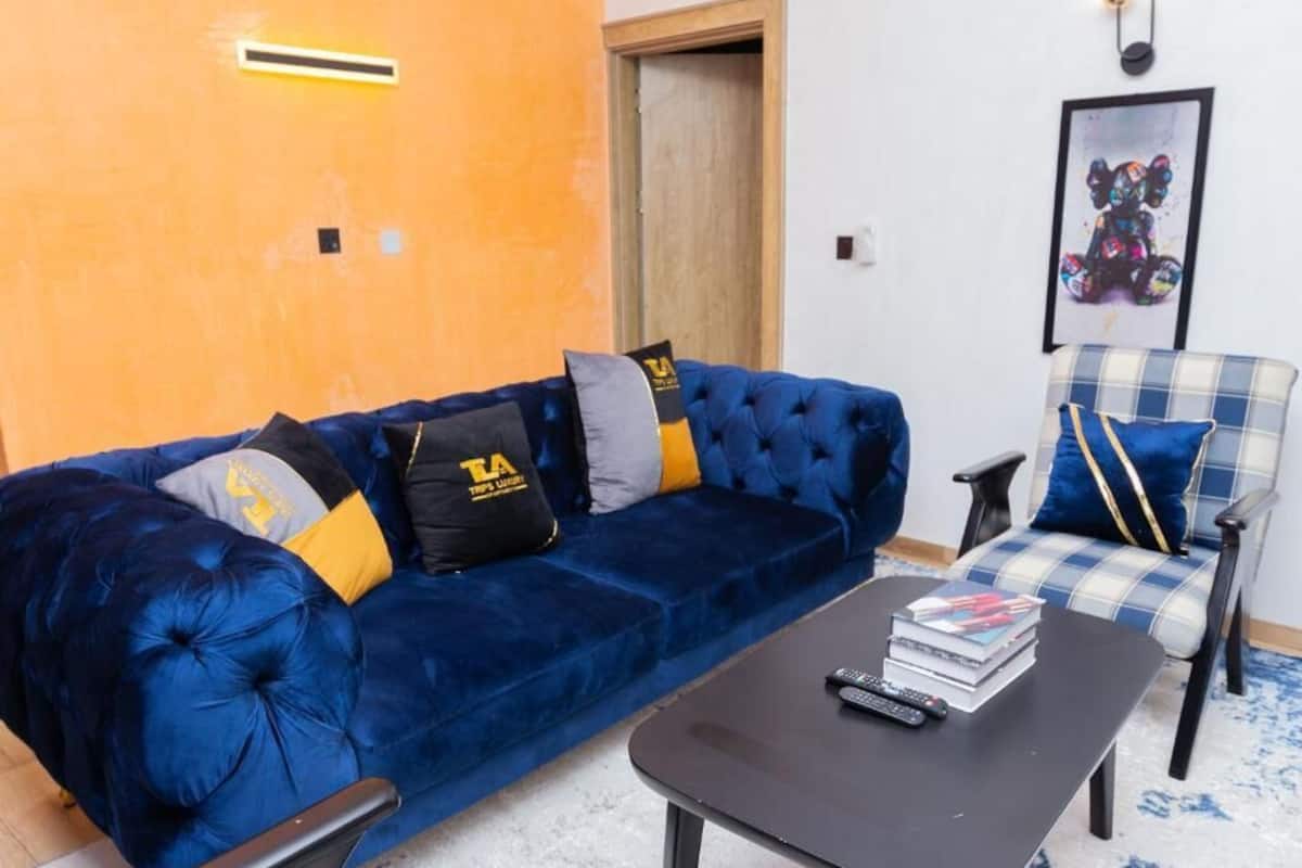 Una sala de estar con un sofá de terciopelo azul, una mesa de centro negra y un sillón de cuadros.
