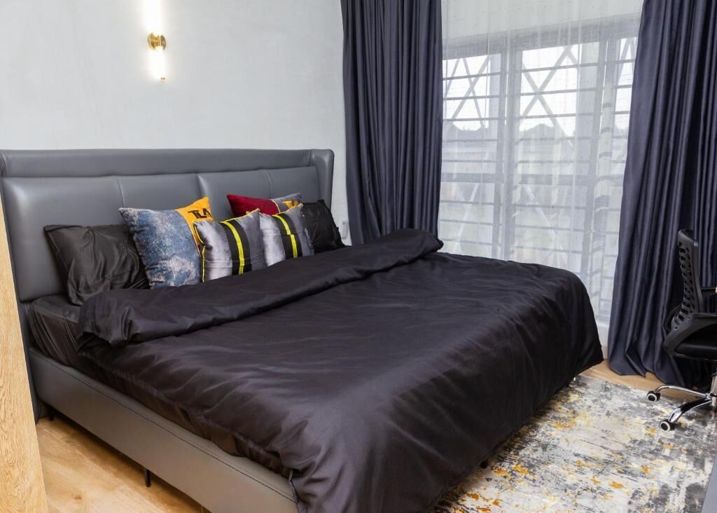 A modern bedroom with a grey upholstered headboard, a black bedspread, and multiple pillows.