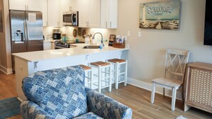 Una cocina moderna con armarios blancos, un refrigerador de acero inoxidable y una barra con taburetes.