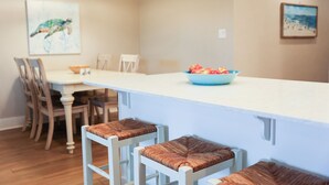 Una cocina moderna con una isla blanca, sillas de madera y un bol de fruta.