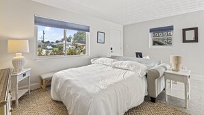 Une chambre à coucher avec un grand lit, une table de chevet avec une lampe, une fenêtre donnant sur l’extérieur et une porte.