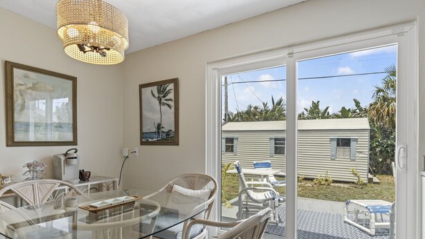 Un coin repas avec une table en verre et des chaises en osier, un lustre et une vue sur une maison, visible à travers une porte-fenêtre coulissante.