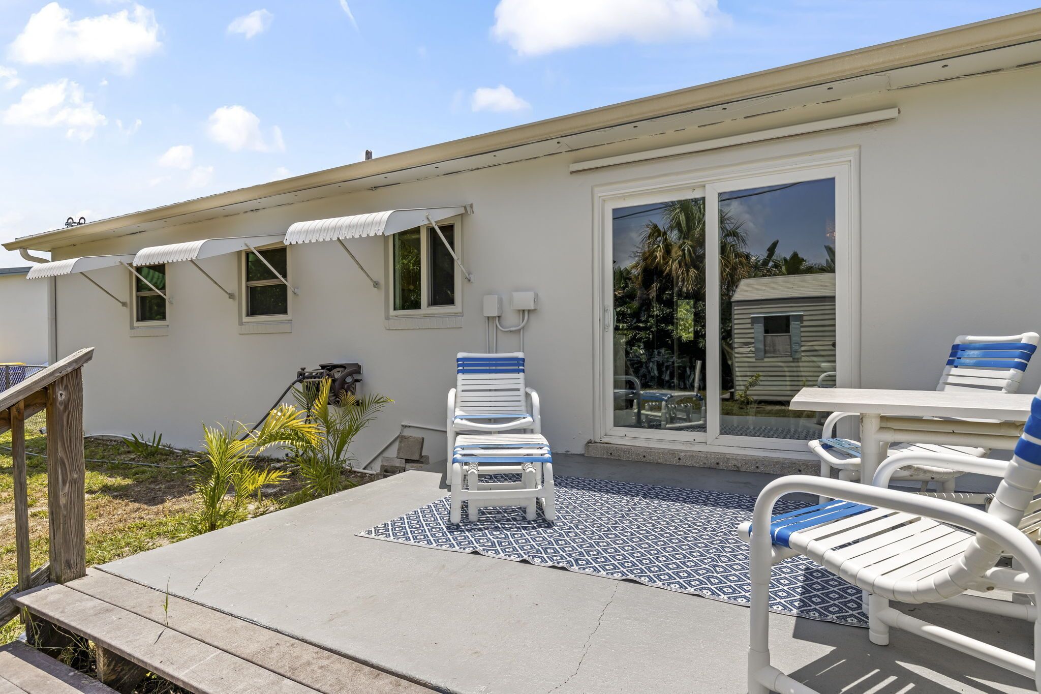 A patio area with a concrete floor, white and blue lounge chairs, a small table, and a covered seating area with a white awning.