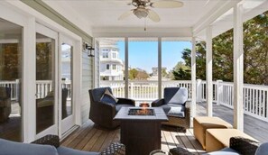A covered porch with a fire pit, seating area, and a view of a white building in the background. - Bethany Village Oceanside Home on Private Beach (Bethany Beach)