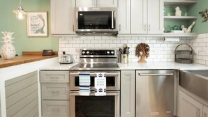 A modern kitchen with stainless steel appliances, white cabinetry, and a green accent wall. - Sea Hag-Heart of Carolina Beach-Private Inground Saltwater Pool (Carolina Beach)
