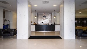 Una zona de recepción con pared de mármol, un mostrador de recepción y dos sofás de cuero negro.