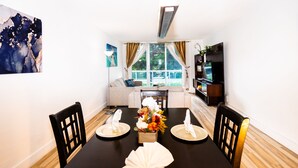 Un comedor con una mesa negra dispuesta para cuatro personas, un sofá y un mueble para televisión al fondo.