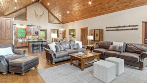 A spacious living area with a wooden ceiling, leather sofas, a coffee table, and a kitchen in the background. - Sugar Mountain Home- Rustic Chic, Hot Tub, Peloton Bike, Free Bus to Ski Resort (Sugar Mountain)