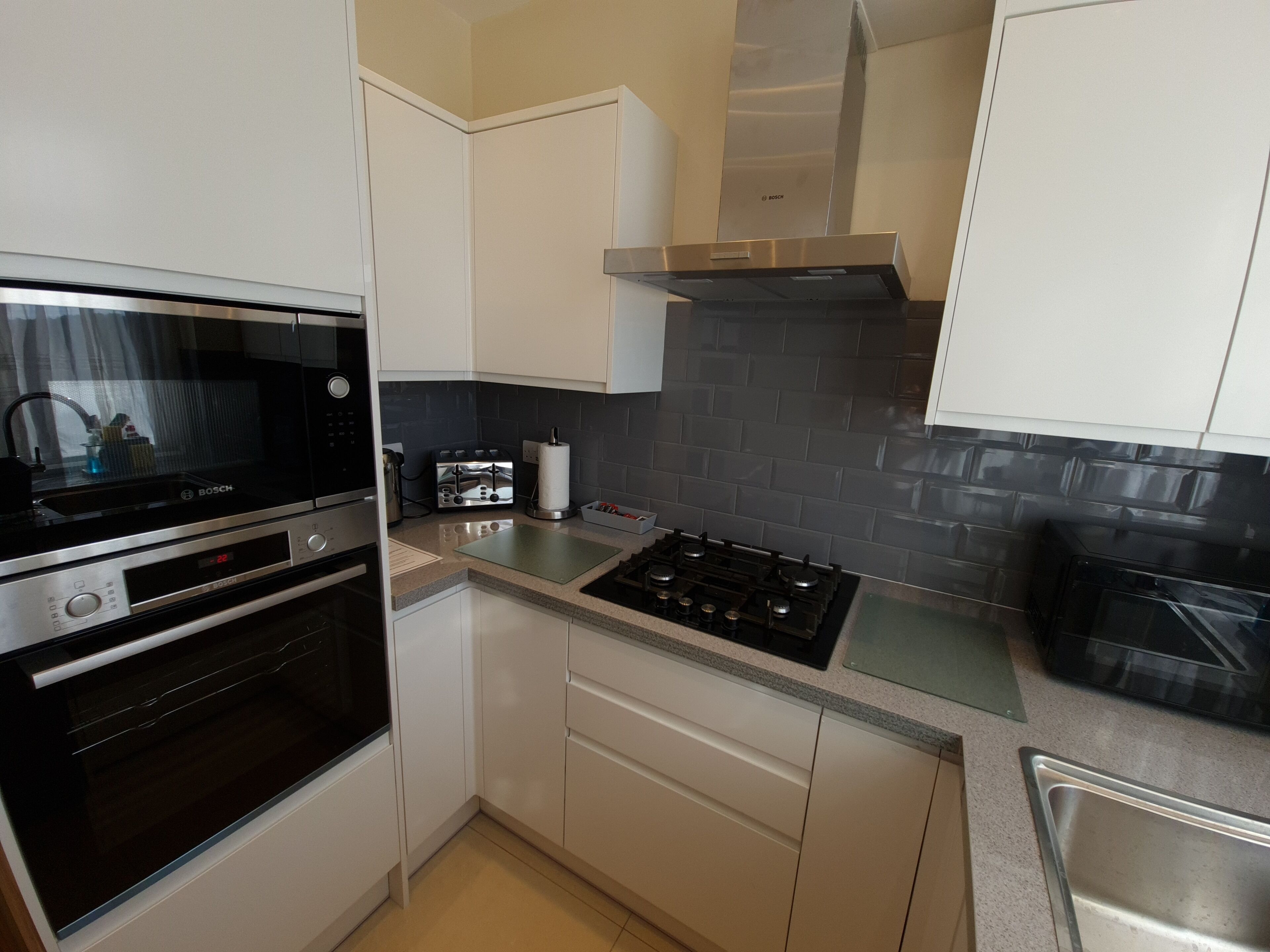 A compact kitchen with a Bosch microwave, oven, toaster, and gas stove.