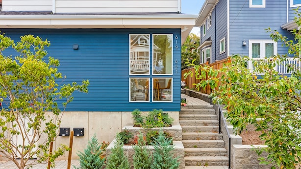 Ein zweistöckiges Haus mit blauer Fassade, einer Veranda mit Treppe und einem kleinen Garten.