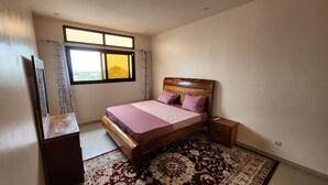 Un dormitori amb llit, una tauleta de nit, un calaixera, una finestra amb cortines i una catifes amb dibuixos.