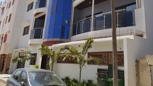 Un edifici de diverses plantes amb balcons, un cotxe a la façana i algunes plantes.