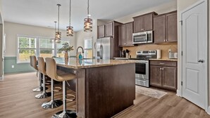 A modern kitchen with dark wood cabinets, stainless steel appliances, and a central island with bar stools. - Pickleball, Arcade & Poker Retreat Near Pinehurst! (Aberdeen)