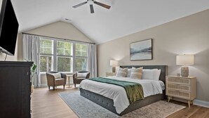 A bedroom with a large bed, a ceiling fan, a TV, a window with curtains, a nightstand, and a dresser. - Pickleball, Arcade & Poker Retreat Near Pinehurst! (Aberdeen)