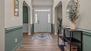 A hallway with a wooden floor, a patterned rug, a white door, and a plant on a shelf. - Pickleball, Arcade & Poker Retreat Near Pinehurst! (Aberdeen)