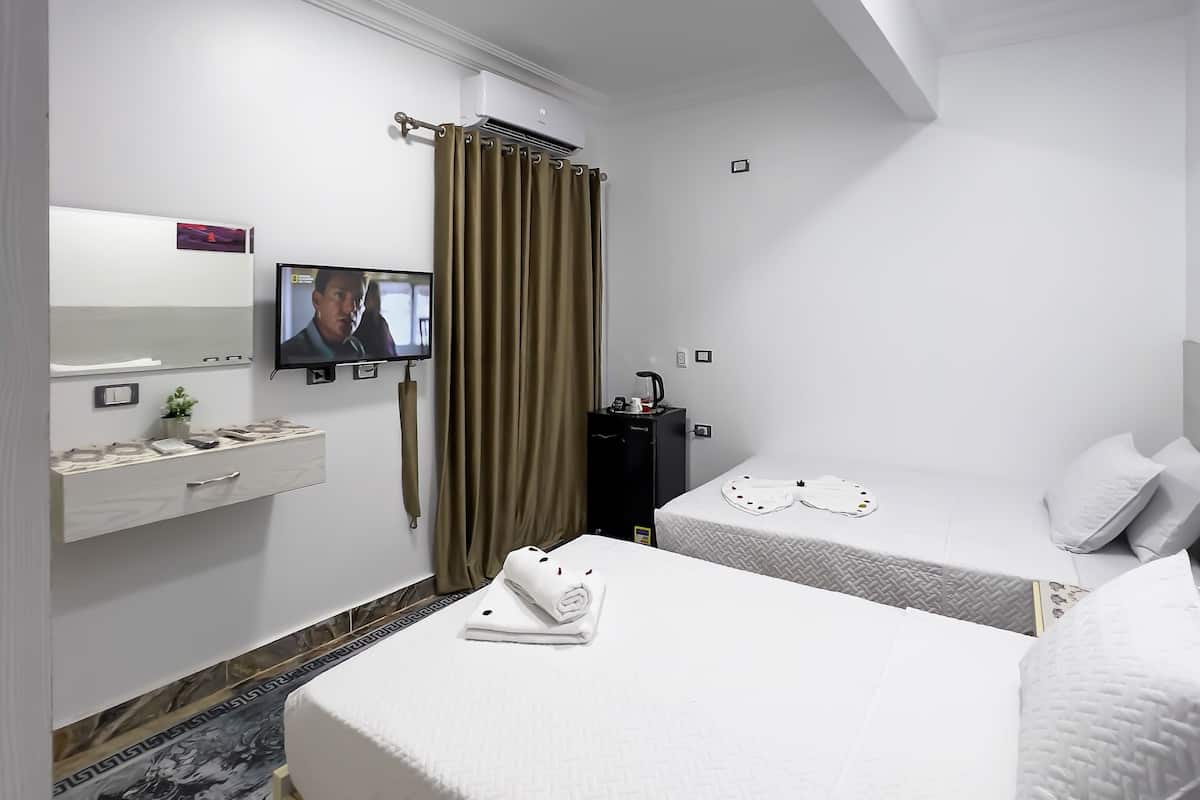 A hotel room with two beds, a TV, a minibar, and a bathroom.