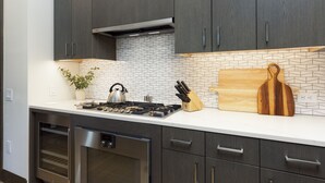 Una cocina moderna con alacenas de madera oscura, un salpicadero de azulejos blancos, una estufa a gas, un hervidor y una tabla de cortar de madera.