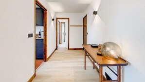 A hallway with a wooden table and a glass sculpture, leading to a kitchen area with a coffee machine.