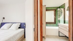 A bedroom with a bed, a bathroom with a bathtub, and a mirror.