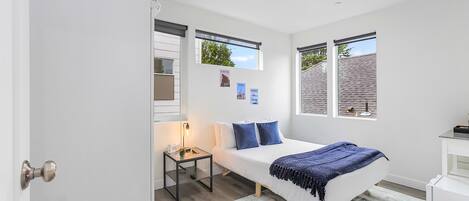 A bedroom with a bed, bedside table, lamp, and two windows.