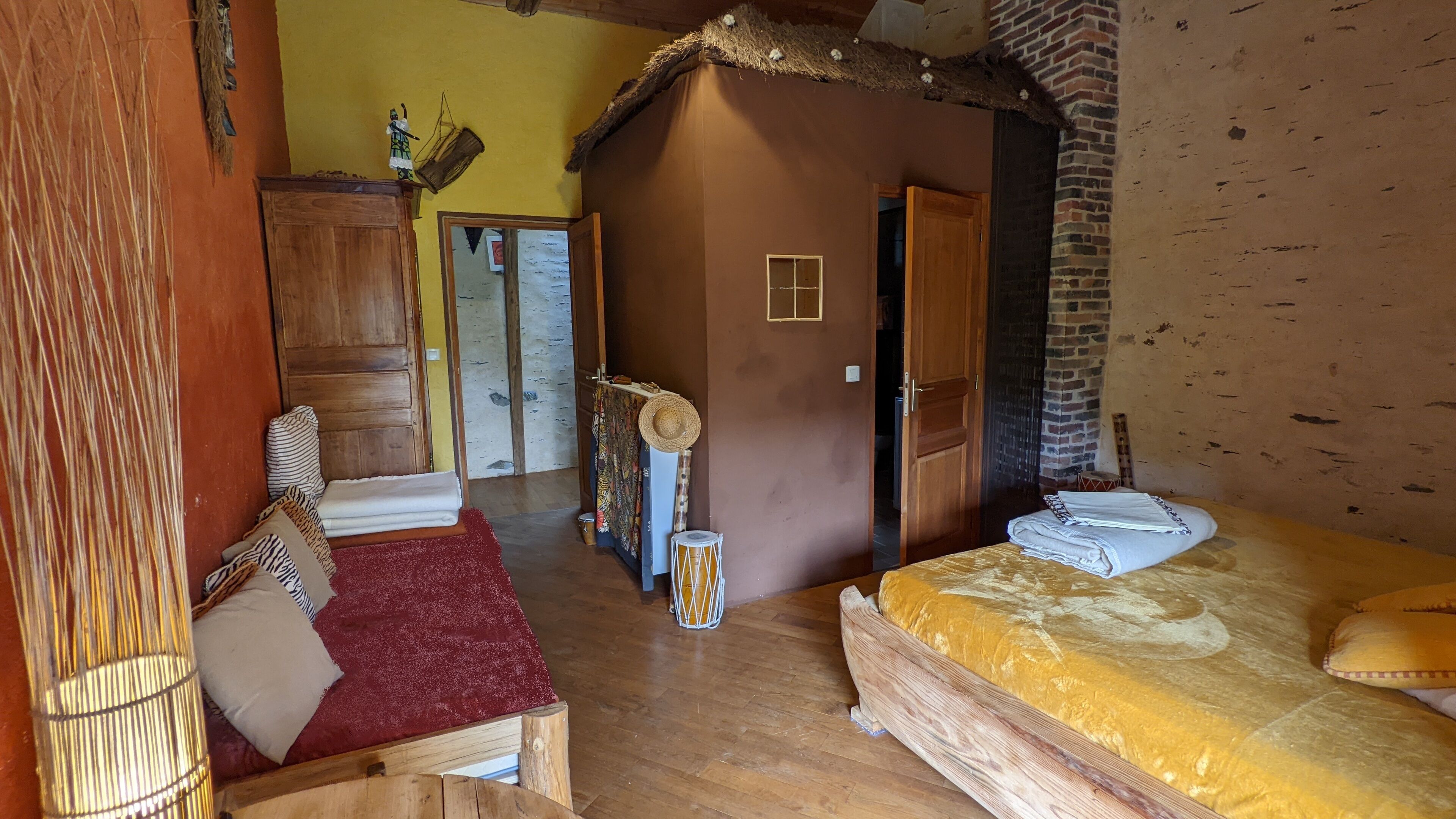 A rustic room with a bed, a wooden cabinet, a red rug, and a straw hat on the wall.