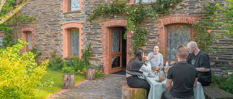 A stone building with a rustic exterior, a wooden door, and a small garden area with a table and chairs.