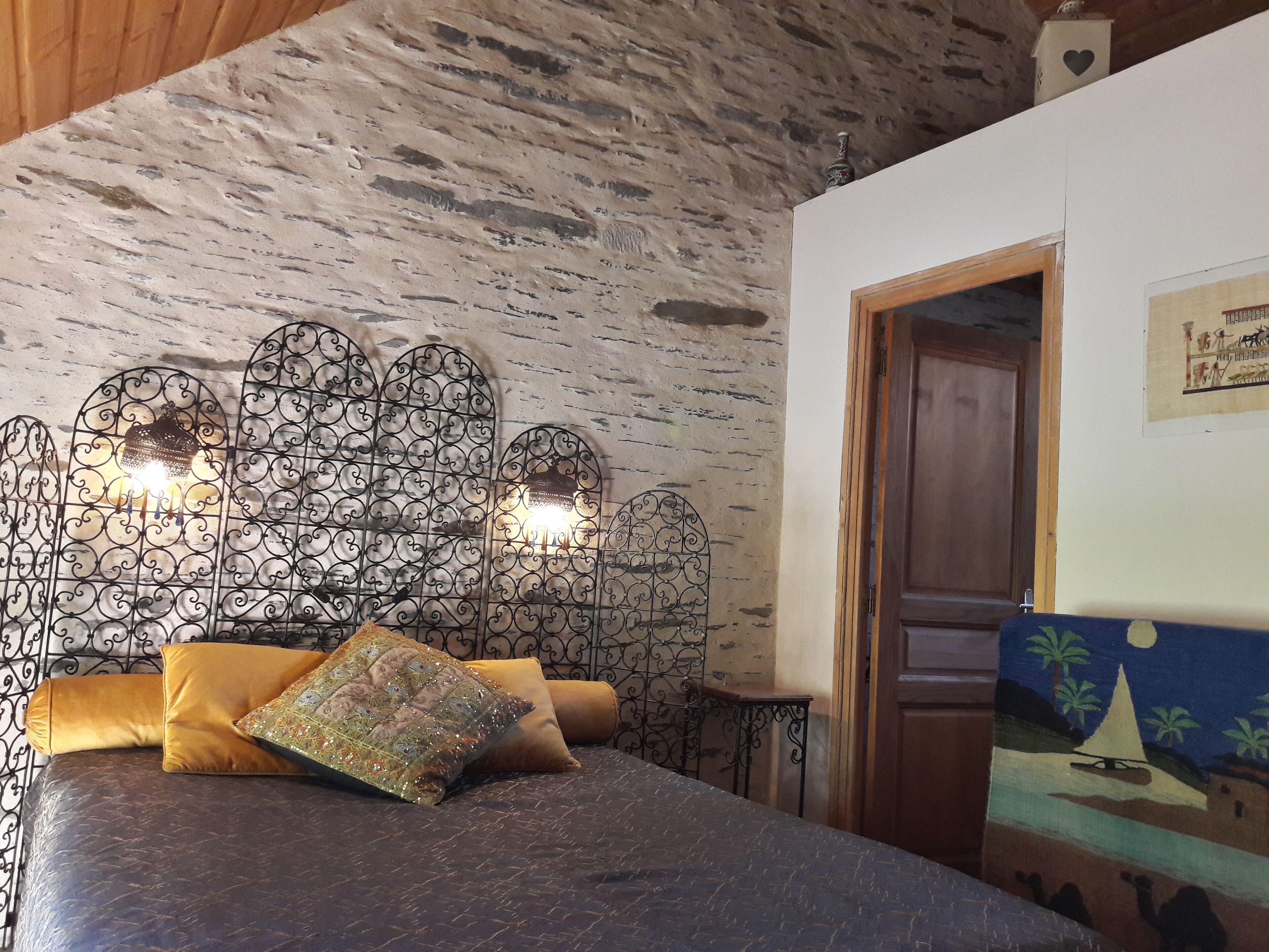 A bedroom with a stone wall, a bed with a patterned pillow, and a decorative metal headboard with lights.