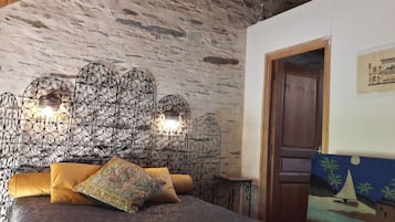 A bedroom with a stone wall, a bed with a patterned pillow, and a decorative metal headboard with lights.